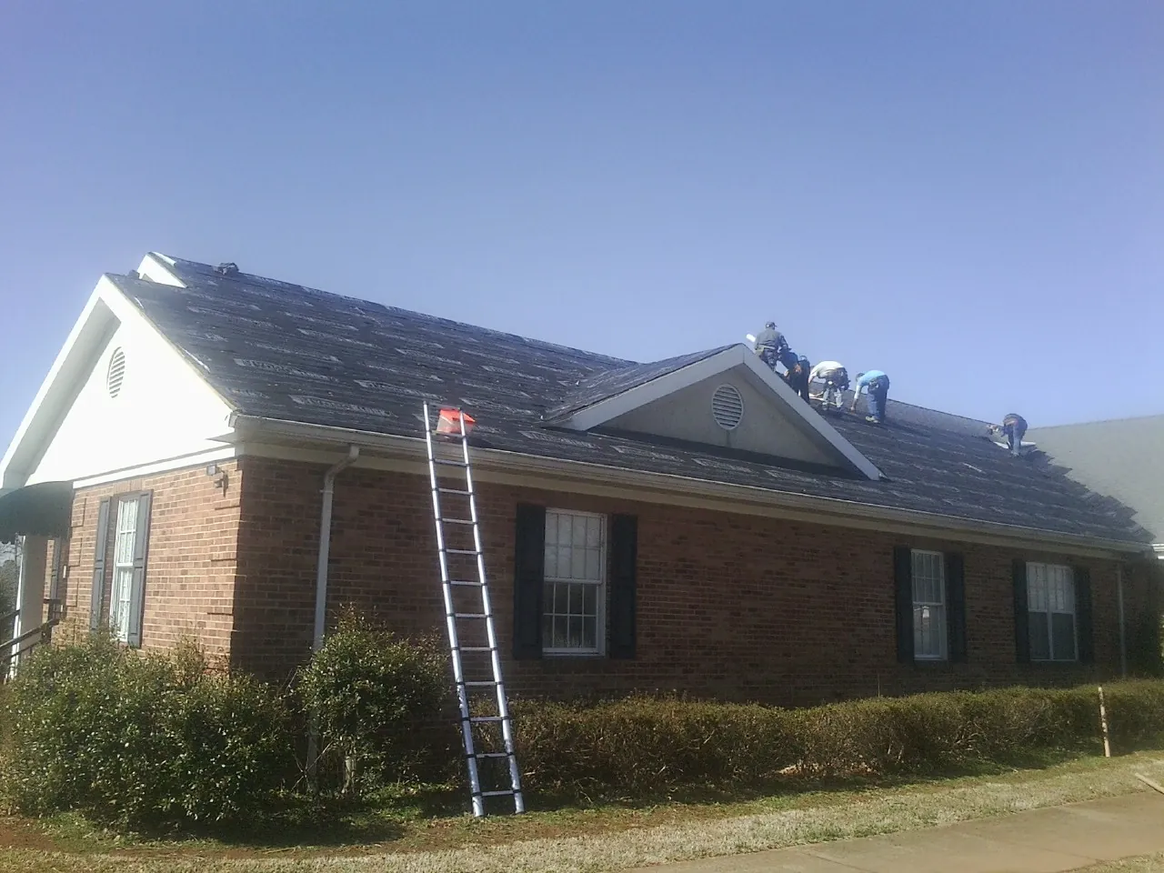 Crew tearing shingles off a brick ranch roof with a ladder set — Emergency Roof Repair work by our crew in Sammamish