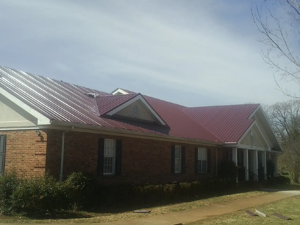Red metal roof with gabled entries on a long brick building, from a Hail Damage Roof Repair job in Sammamish