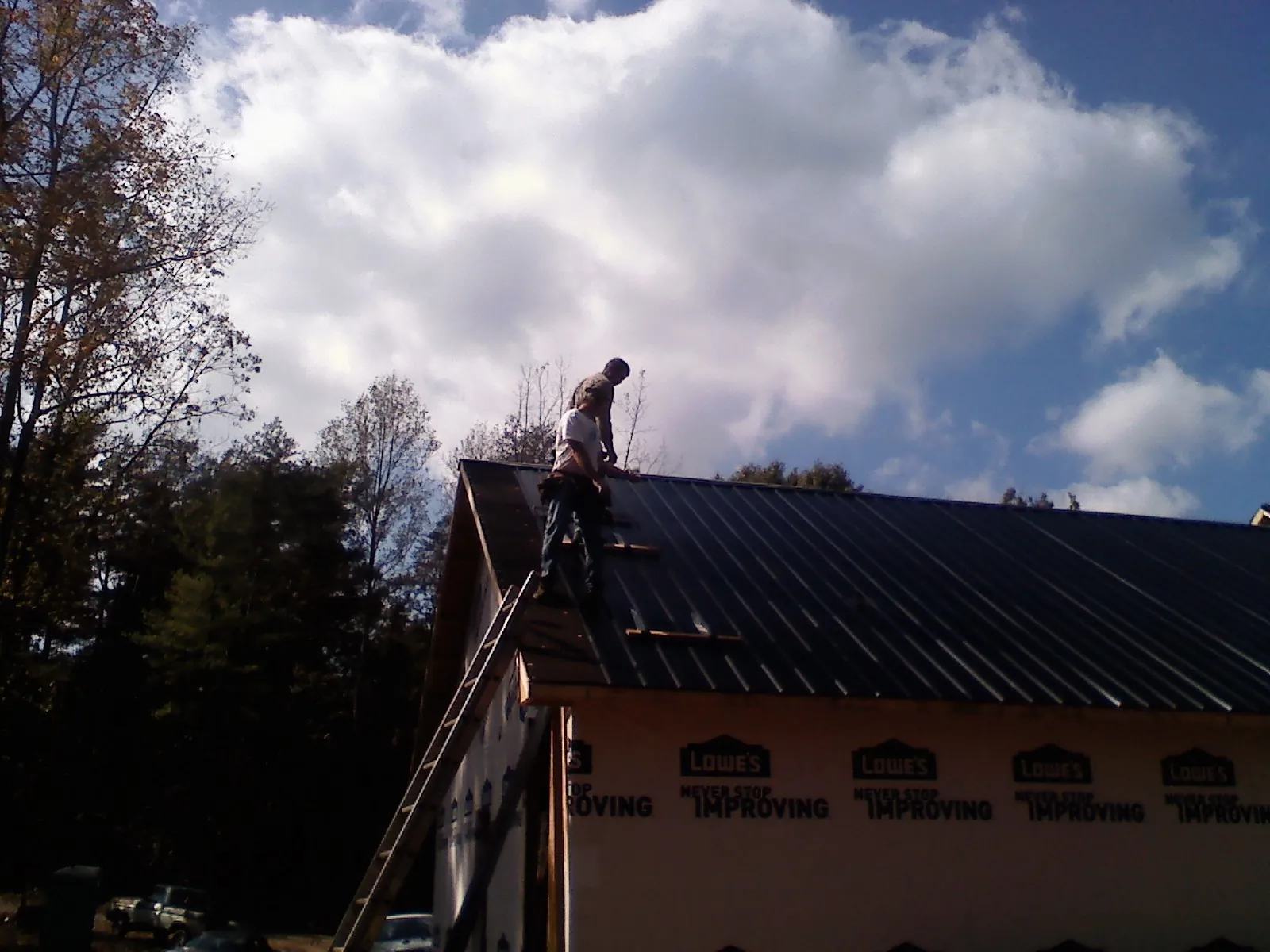 Roofer fastening dark metal panels high against a cloudy sky, from a Roof Inspection job in Sammamish
