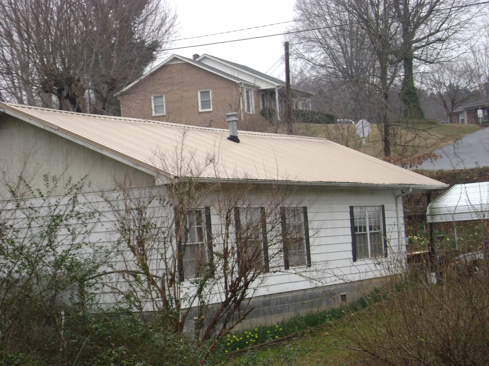 Tan metal roof on a white sided house set into a hillside — Commercial Roofing by Roofing Brothers in Sammamish